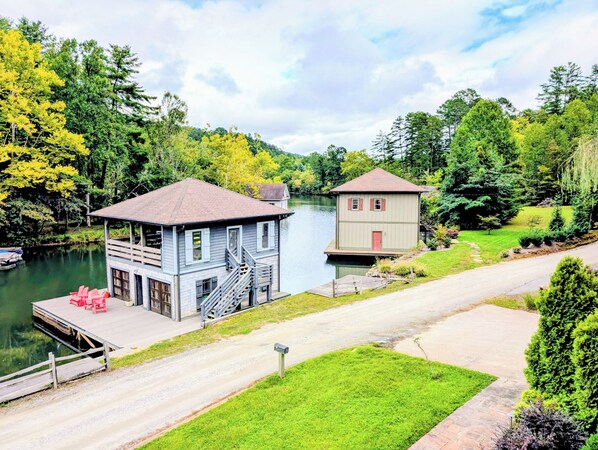 A two-story house with a dock, a small boat, and a grassy yard.