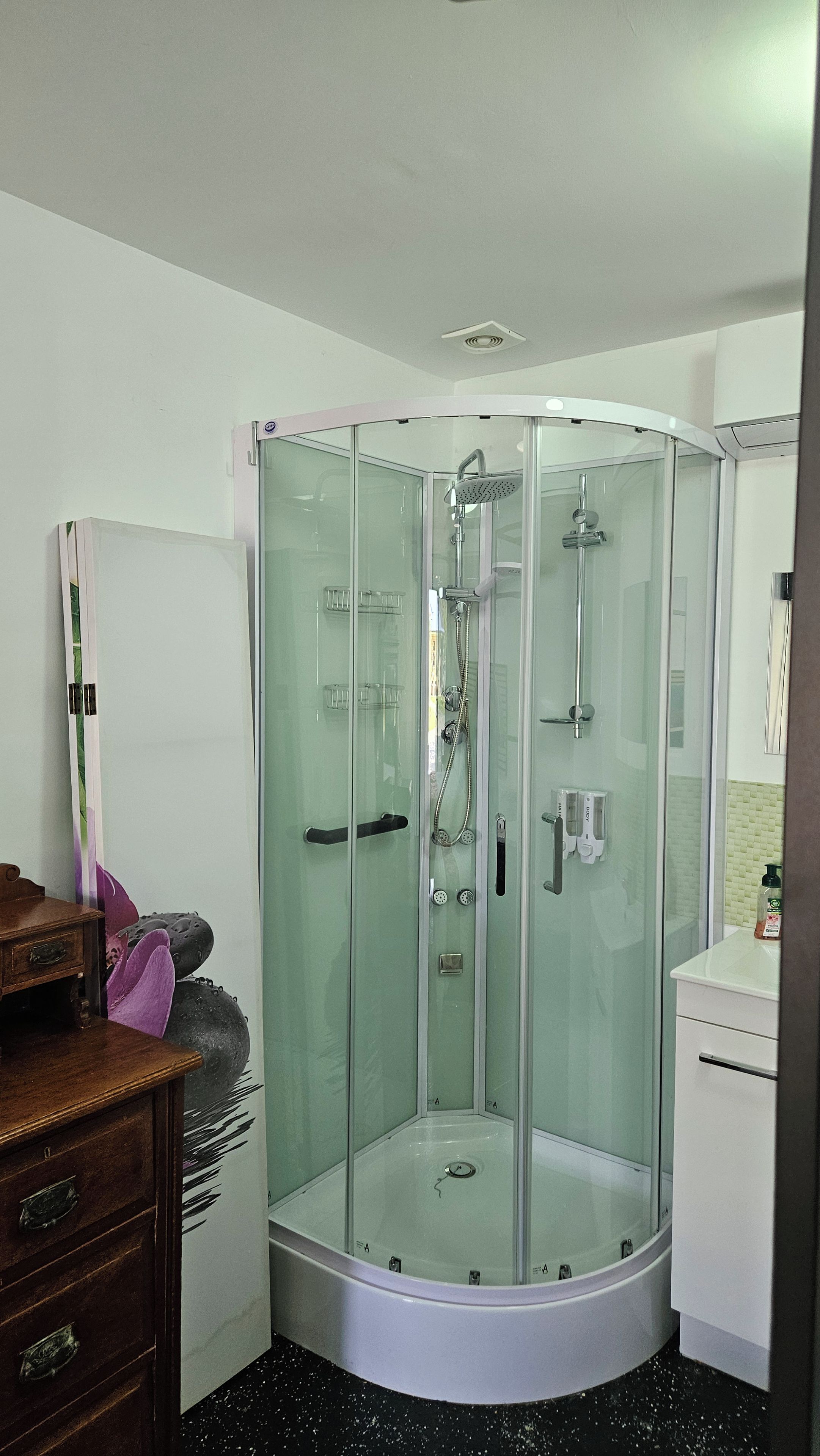 A glass-enclosed shower stall with a handheld showerhead and a wall-mounted faucet.