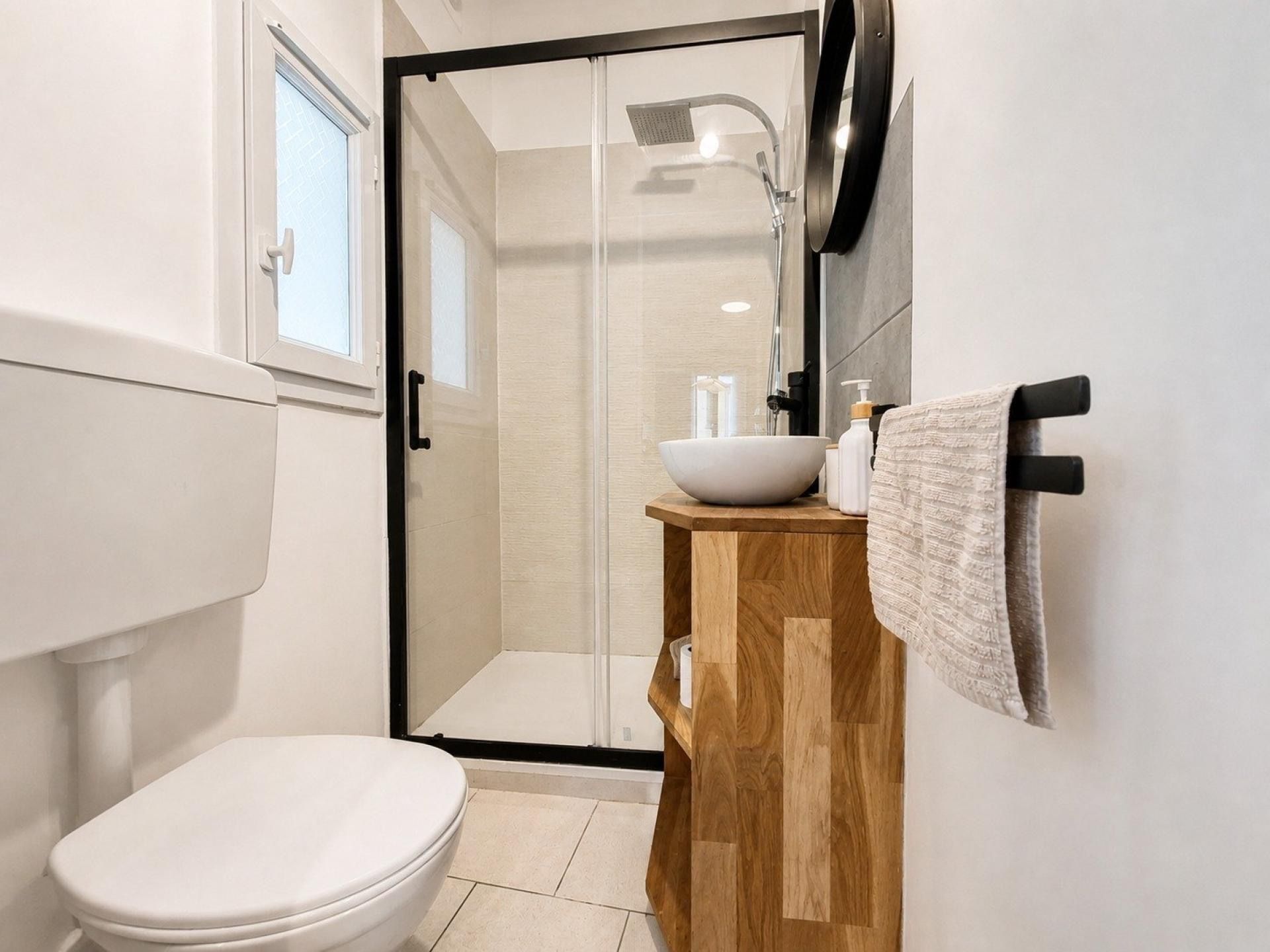 Ein modernes Badezimmer mit Toilette, einem Holzbadezimmerschrank, einer Duschkabine aus Glas und einem Handtuchhalter.