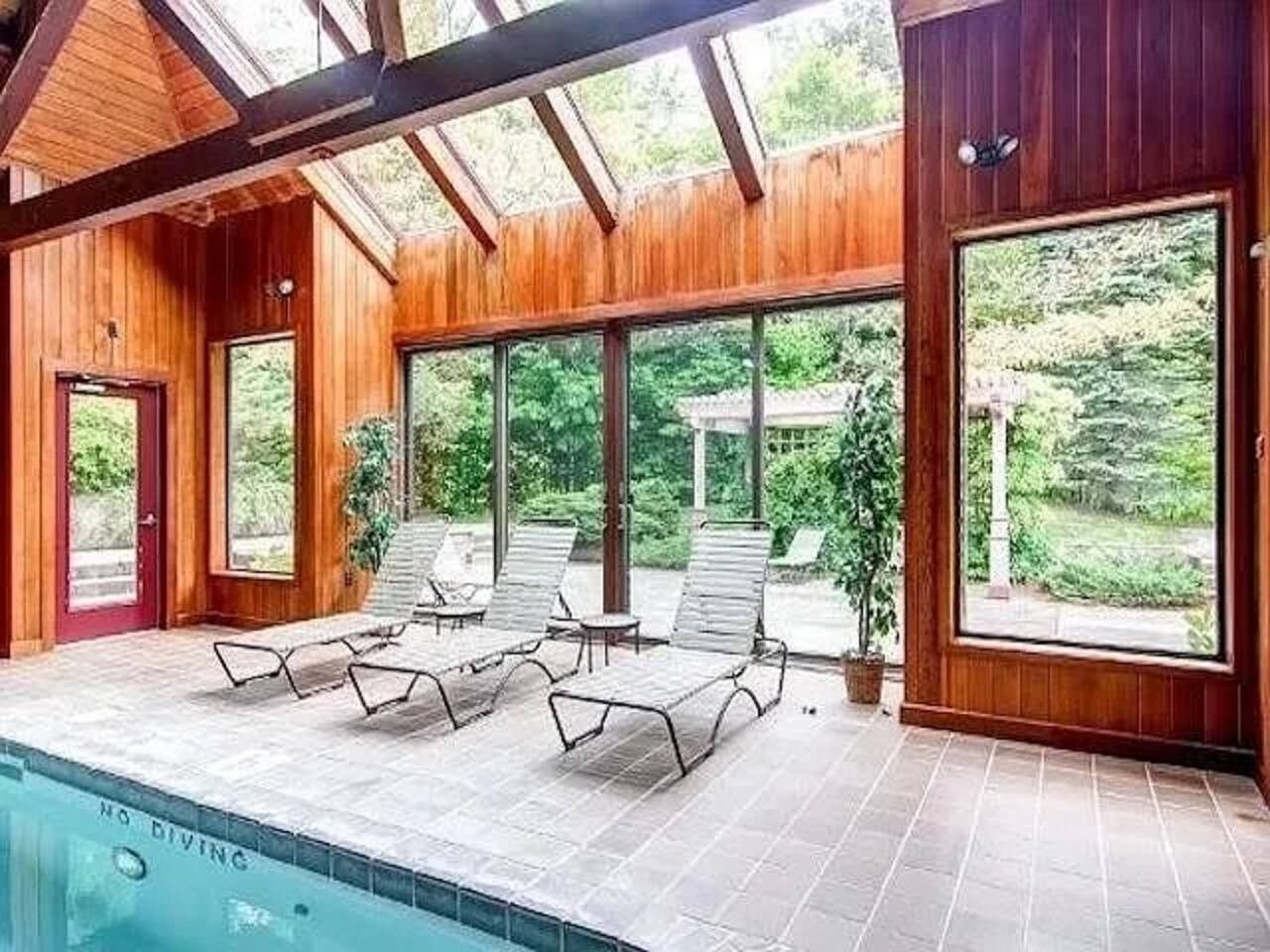 Ein Poolbereich mit Liegestühlen und einer Pergola, umgeben von Holzwänden und großen Fenstern.