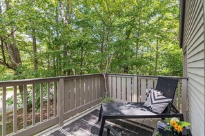 Une terrasse en bois avec une chaise noire et une petite table, entourée d’arbres.