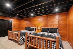 A room with two wooden beds, a black door, and a ceiling with exposed beams and lighting fixtures. - Private Cabin Retreat | near Stratton & Mt. Snow (Jamaica)