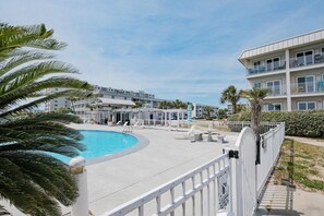 Un complex turístic amb piscina, gandules i un edifici de diversos pisos amb balcons.