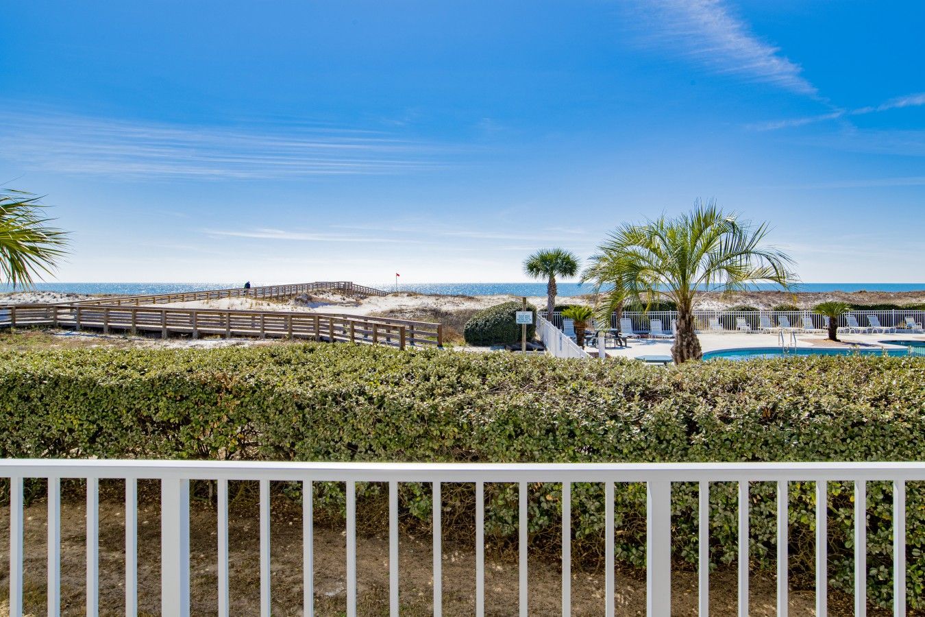 A beachfront property with a wooden boardwalk, a swimming pool, and a view of the ocean.
