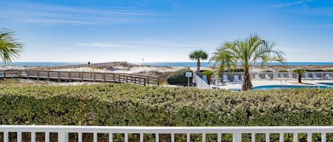A beachfront property with a wooden boardwalk, a swimming pool, and a view of the ocean.