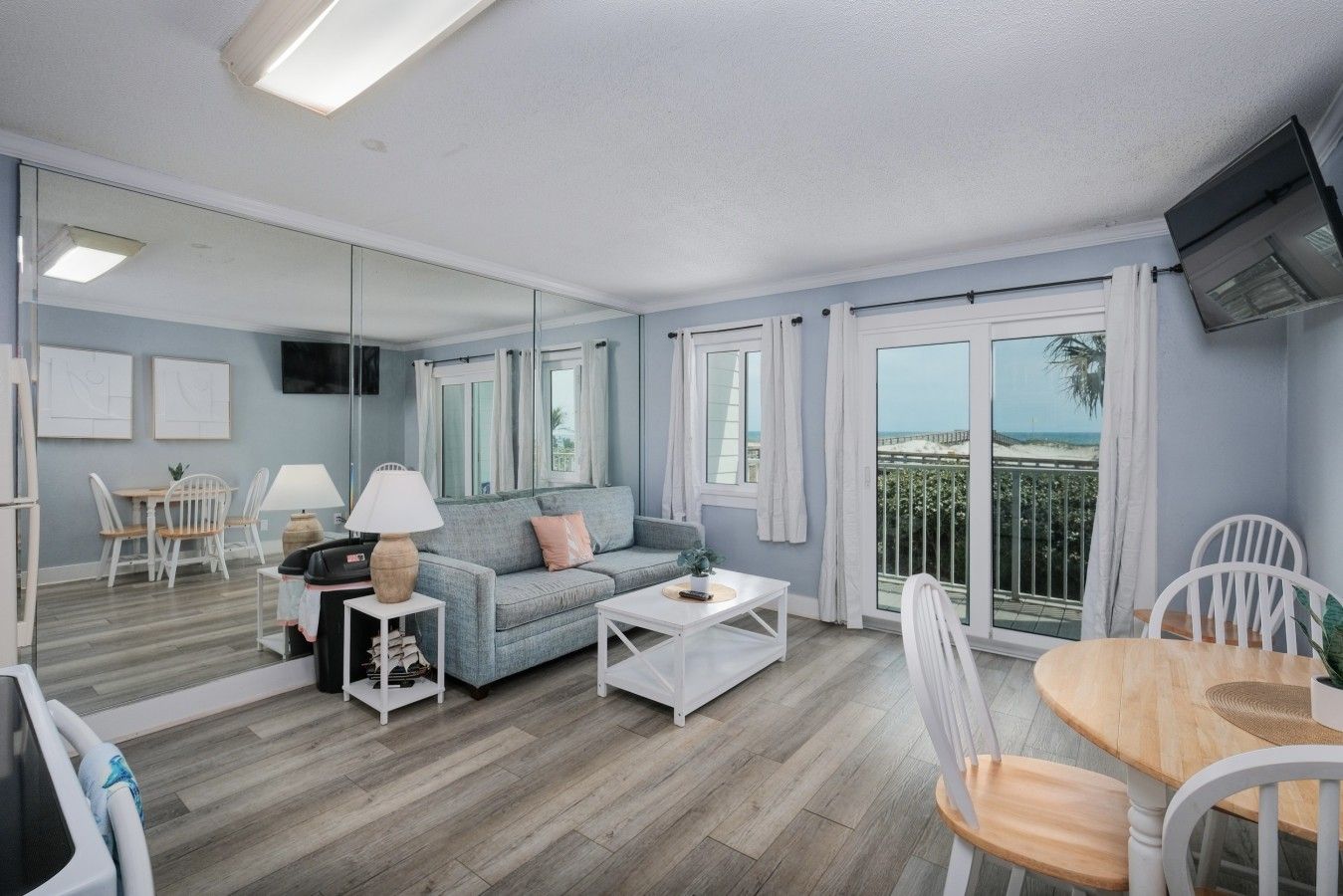 A modern living room with a sofa, coffee table, and chairs, a dining area with a table and chairs, and a balcony with a view.