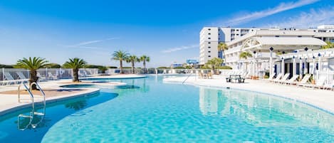 Una piscina azul cristalina con sillas de descanso y palmeras, rodeada por un edificio blanco con balcones.
