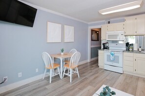 Een moderne keuken met witte kasten, een inbouwoven en een eethoek met een ronde tafel en vier stoelen.