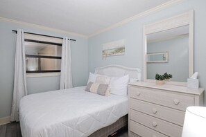 Quarto com cama, penteadeira, espelho e janela com cortinas.