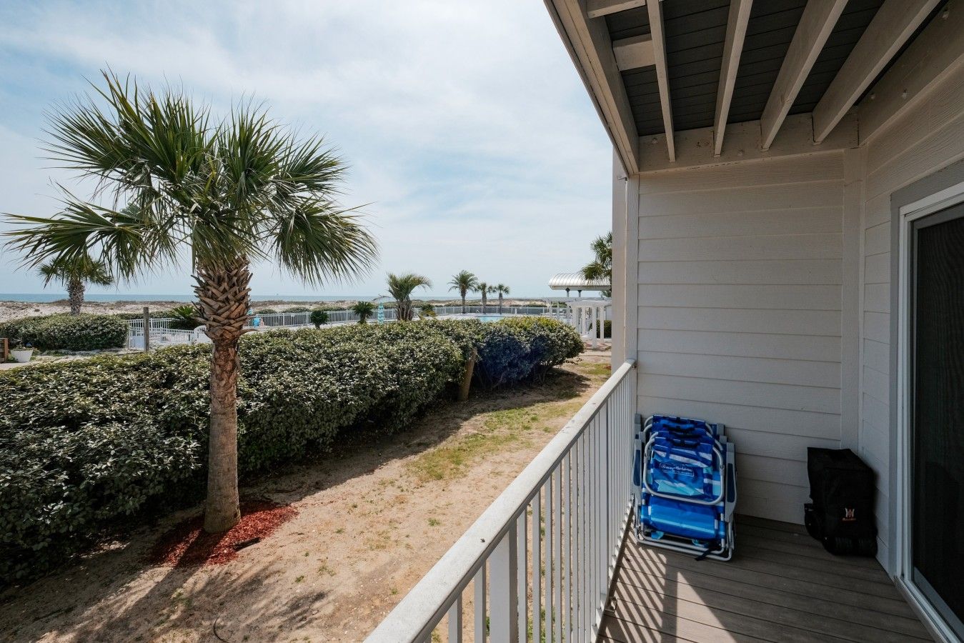 Ein Balkon mit Blick auf den Strand, eine Palme und eine Hecke.