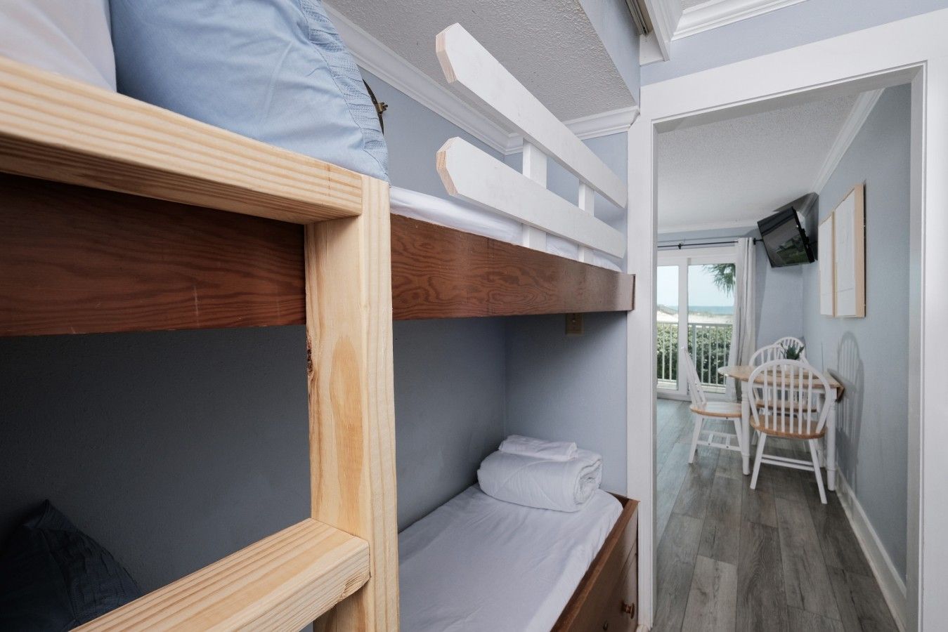 A bunk bed room with a small table and chair, a television, and a balcony with a view.