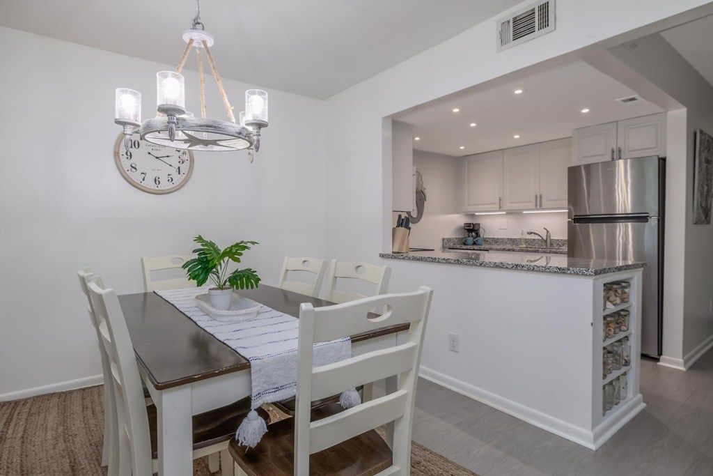 A modern kitchen with white cabinetry, a stainless steel refrigerator, and a dining area with a wooden table and white chairs.