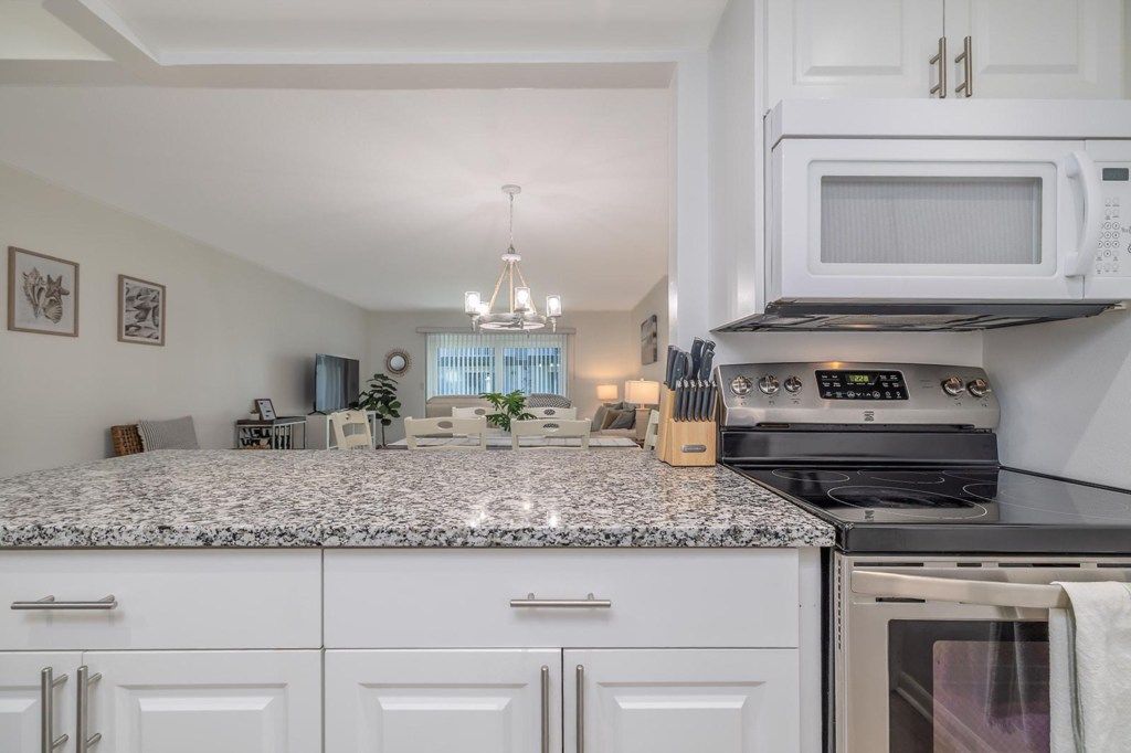 A kitchen with white cabinetry, a granite countertop, a built-in stove, and a microwave.