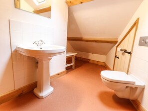 A bathroom with a pedestal sink, toilet, and a wooden-framed window. - Llys Gwaun (Fishguard)