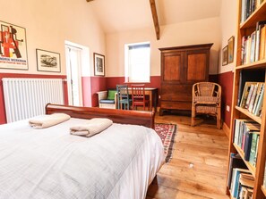 A bedroom with a bed, a wooden cabinet, a chair, and a bookshelf. - Llys Gwaun (Fishguard)