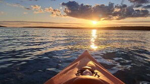 Un kayak sobre el agua con un atardecer de fondo.