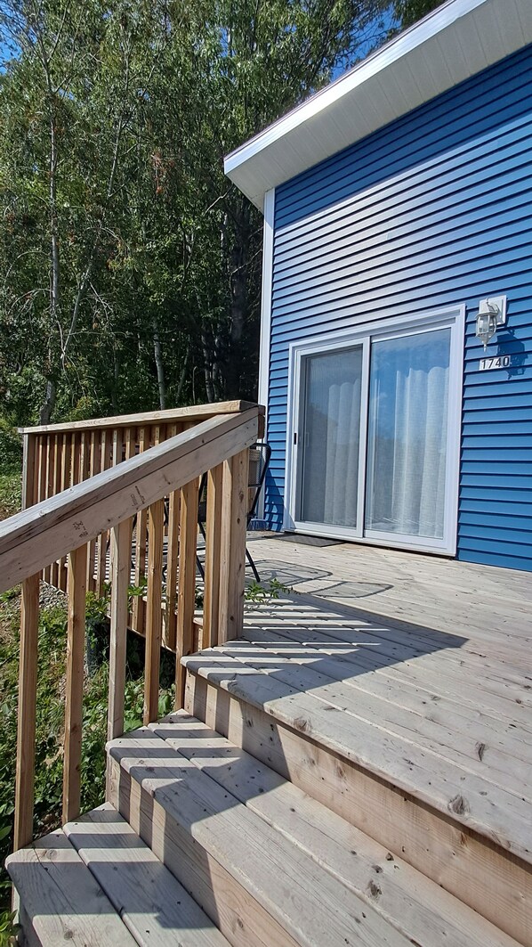 A wooden deck leading to a blue house with a sliding glass door and a mailbox.