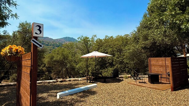 A gravel area with a wooden bench, a picnic table, and an umbrella. - Luxury Camper Van Parking - 16 miles to Yosemite 5 miles to Bass Lake! #3 (Oakhurst)