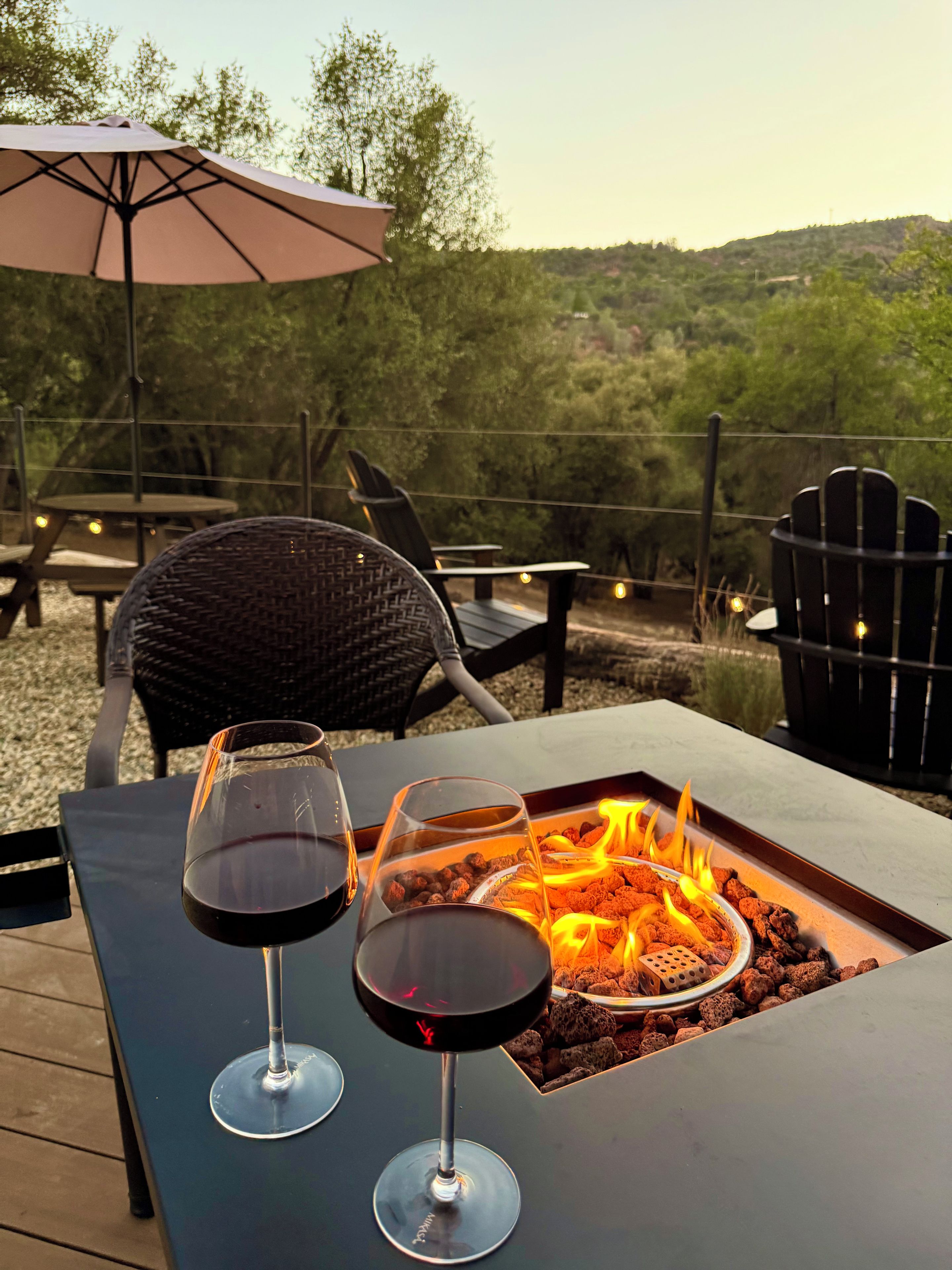 Une table avec deux verres à vin et un foyer, entourée de sièges d’extérieur et offrant une vue sur les arbres et les collines.
