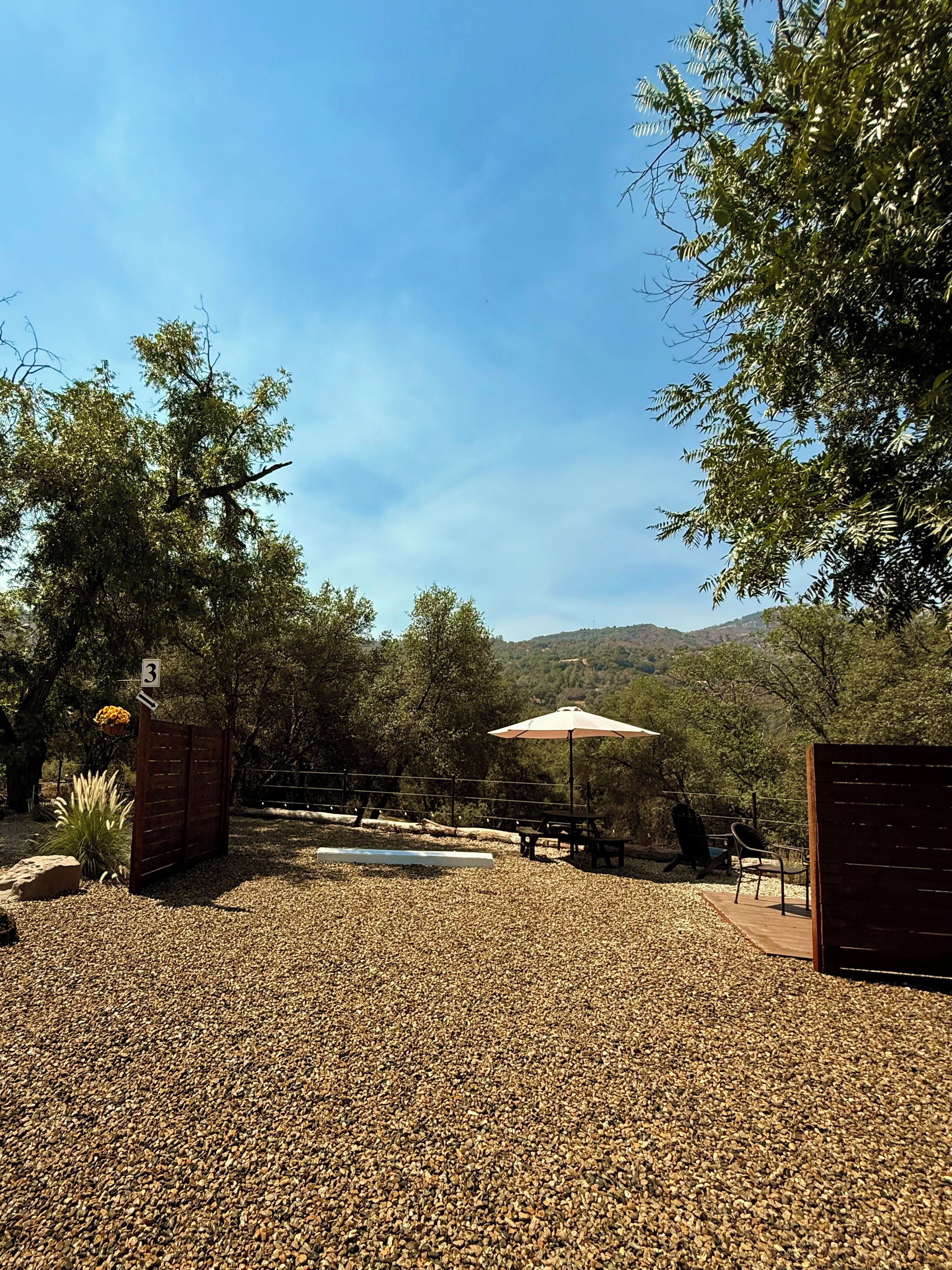 An outdoor patio area with a gravel surface, a picnic table, a bench, and an umbrella.