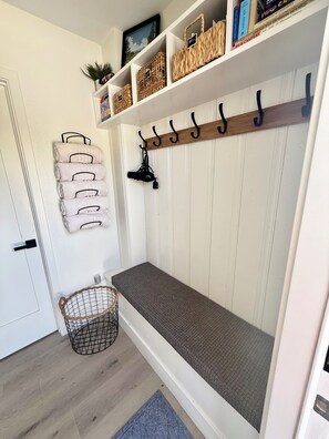 A room with a bench, a coat rack, a basket, and a door.