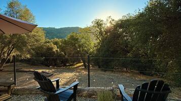 An outdoor seating area with Adirondack chairs, a wooden table, and a gravel ground.