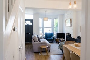 A modern living room with a sofa, armchair, and a TV. There is a dining table with chairs and a fireplace. - 🏖️ Seaside Charm in Broadstairs – Cosy 2-Bed Home with Private Parking (Broadstairs)