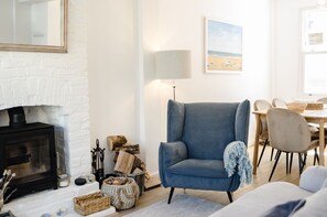 A cozy living room with a fireplace, a blue armchair, and a dining area with a table and chairs. - 🏖️ Seaside Charm in Broadstairs – Cosy 2-Bed Home with Private Parking (Broadstairs)