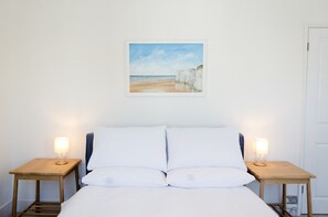 Ein Schlafzimmer mit einem Bett, zwei Nachttischen und einem Bilderrahmen mit einer Ansicht vom Strand.