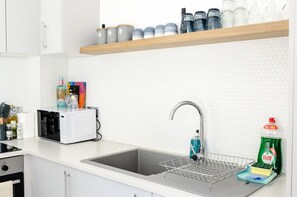 Et køkken med indbygget mikrobølgeovn, en vask med sæbedispenser og en hylde med diverse beholdere.