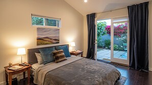 A bedroom with a large bed, two bedside tables, a nightstand, a window with a view of greenery, and a sliding glass door to an outdoor area. - Private, designer furnished, freestanding 1 bedroom ADU in Los Angeles (Los Angeles)