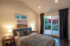 A bedroom with a large bed, two bedside tables, a nightstand, a window with a view of greenery, and a sliding glass door to an outdoor area. - Private, designer furnished, freestanding 1 bedroom ADU in Los Angeles (Los Angeles)