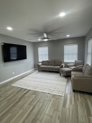 A living room with a flat-screen TV, beige sofas, a patterned rug, and wooden flooring. - Newly Renovated - Sleek & Modern Minimalist 3BR/2BA House (Del Rio)
