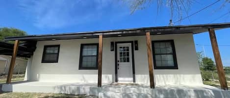 A single-story house with a flat roof, a front porch, and a door with a window above it.