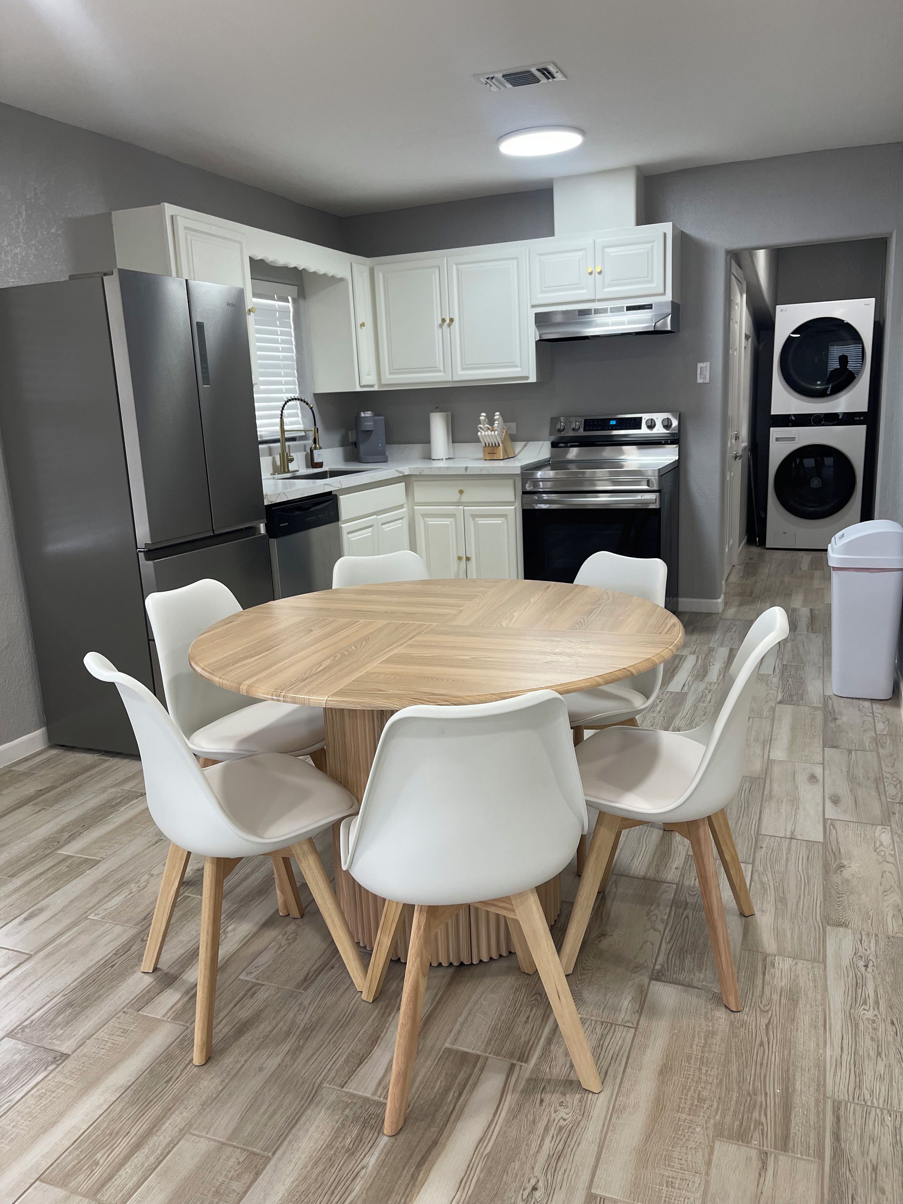 A modern kitchen with white cabinets, stainless steel appliances, and a round wooden table with white chairs.