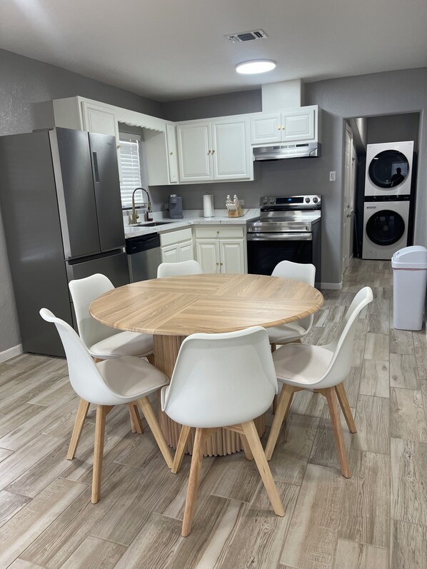 A modern kitchen with white cabinets, stainless steel appliances, and a round wooden table with white chairs.