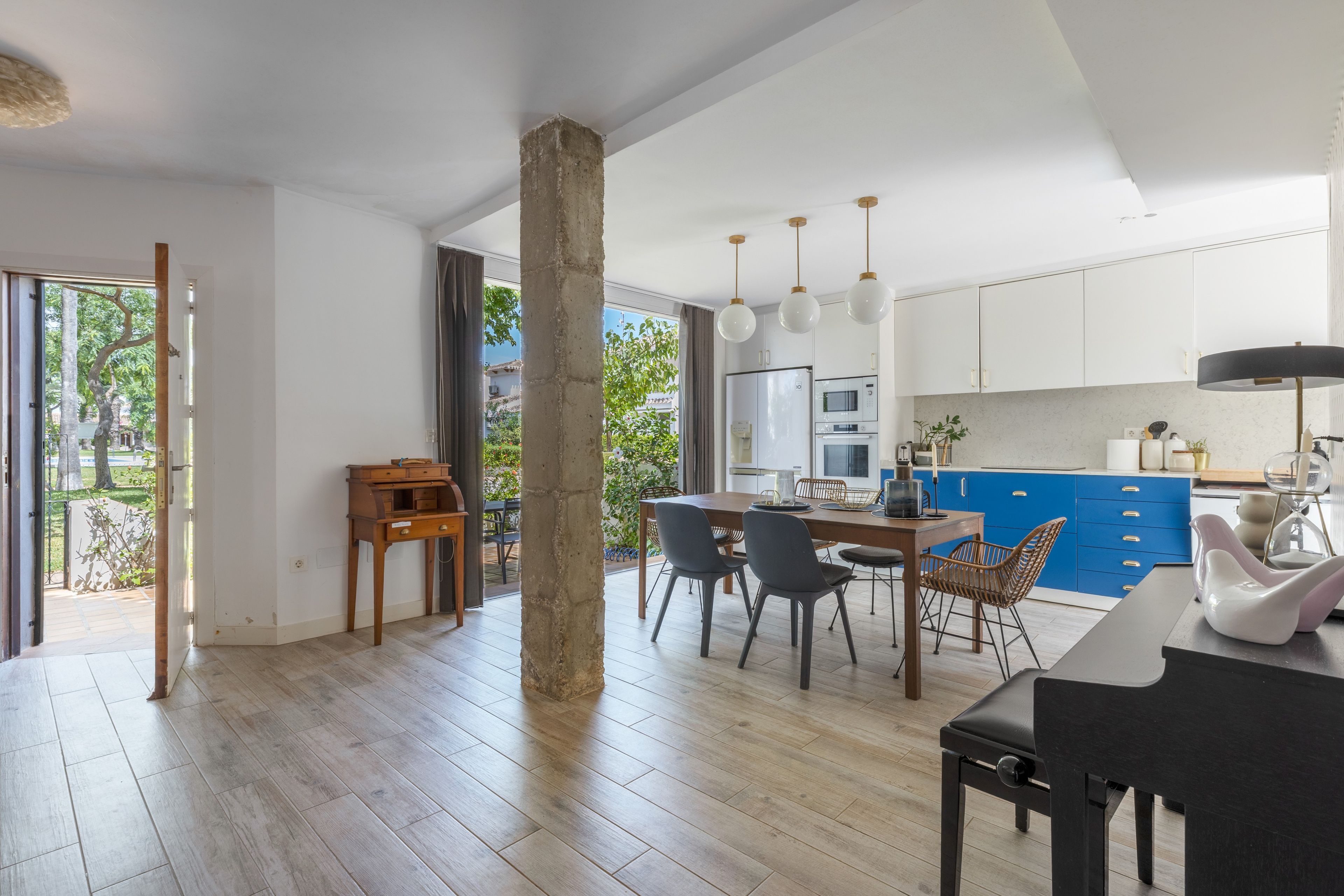 Eine geräumige Küche mit modernen Geräten, ein Essbereich mit einem Holztisch und -stühlen sowie ein großer, offener Raum mit einer Betonstütze.