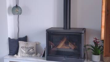 A modern living room with a built-in wood-burning stove, a bench with cushions, a hanging lamp, and a potted plant.
