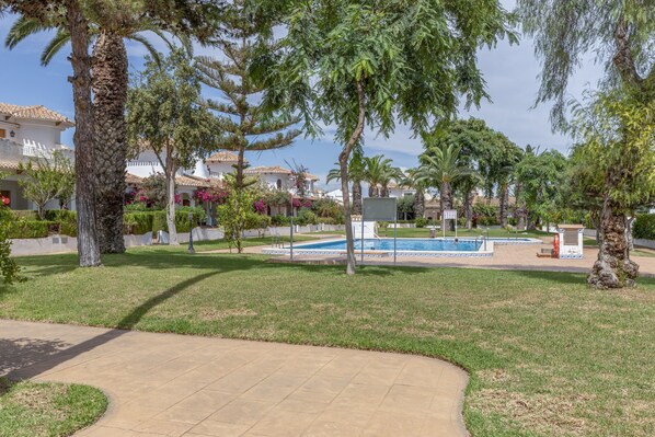 A pool area with a tiled deck, surrounded by palm trees and a building with a tiled roof.
