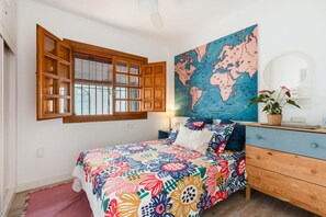 Ein Schlafzimmer mit einem Holsterfenster, einem Bett mit bunter Blumenbettwäsche, einer Weltkarte an der Wand und einer Kommode mit Spiegel.