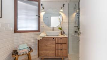 Un baño con tocador de madera, espejo redondo y cabina de ducha con mampara de vidrio.