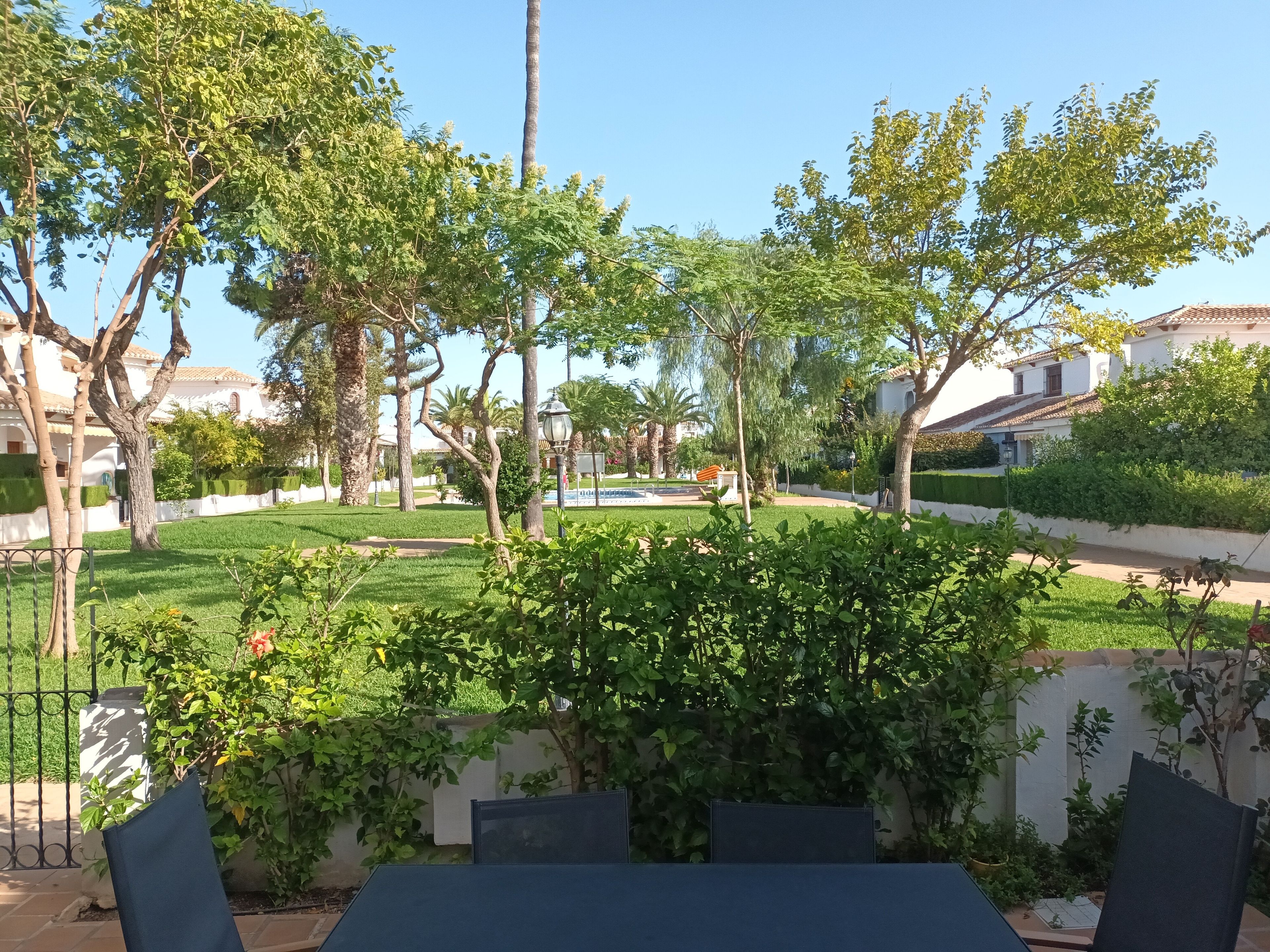 Une cour avec une pelouse, des arbres et un bâtiment blanc doté d’un toit recouvert de tuiles.