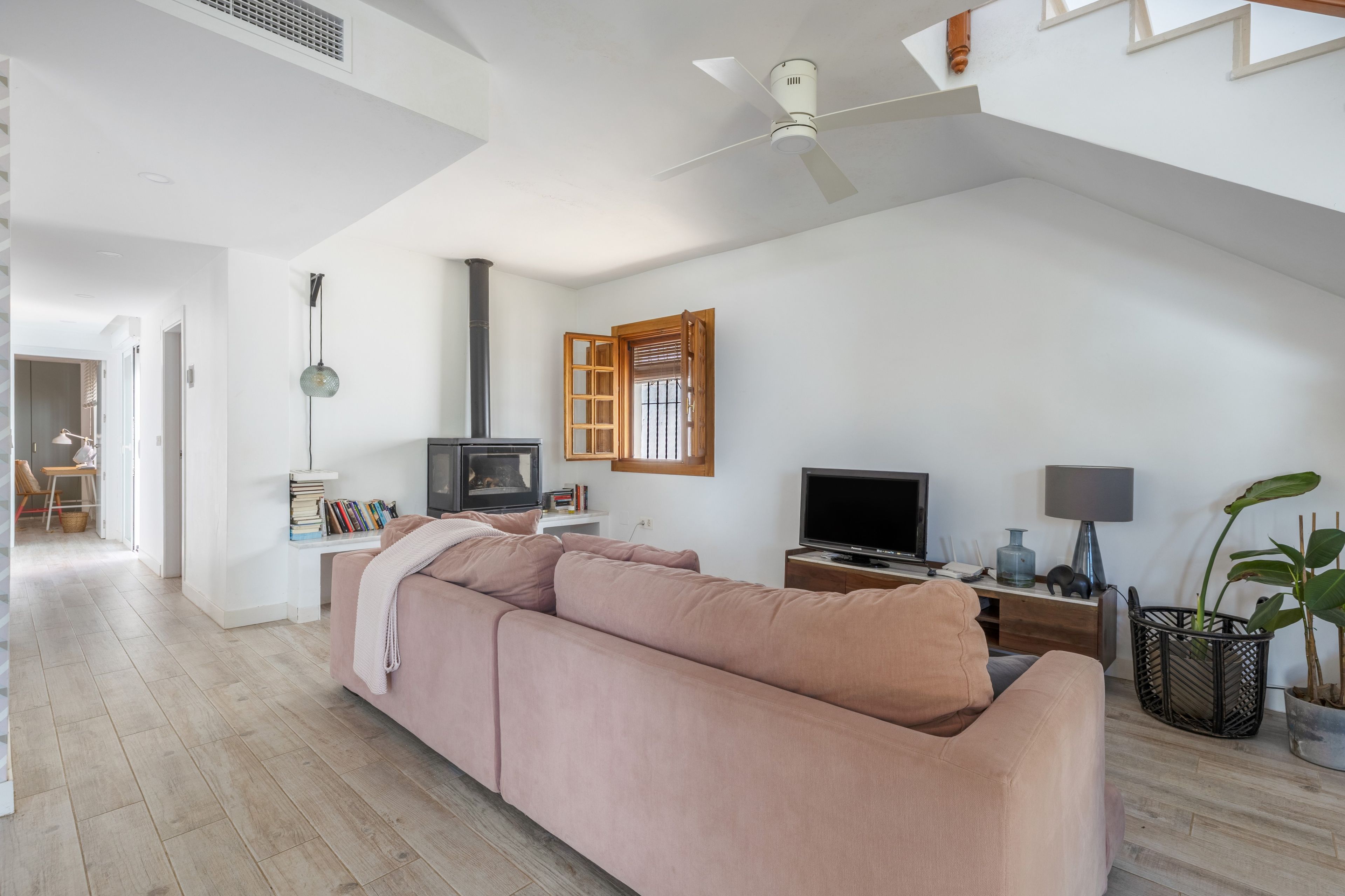 Un salón amplio con un sofá rosa grande, un televisor, una chimenea y un ventilador de techo.