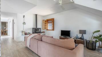 Un salón amplio con un sofá rosa grande, un televisor, una chimenea y un ventilador de techo.