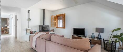 A spacious living room with a large pink sofa, a television, a fireplace, and a ceiling fan.