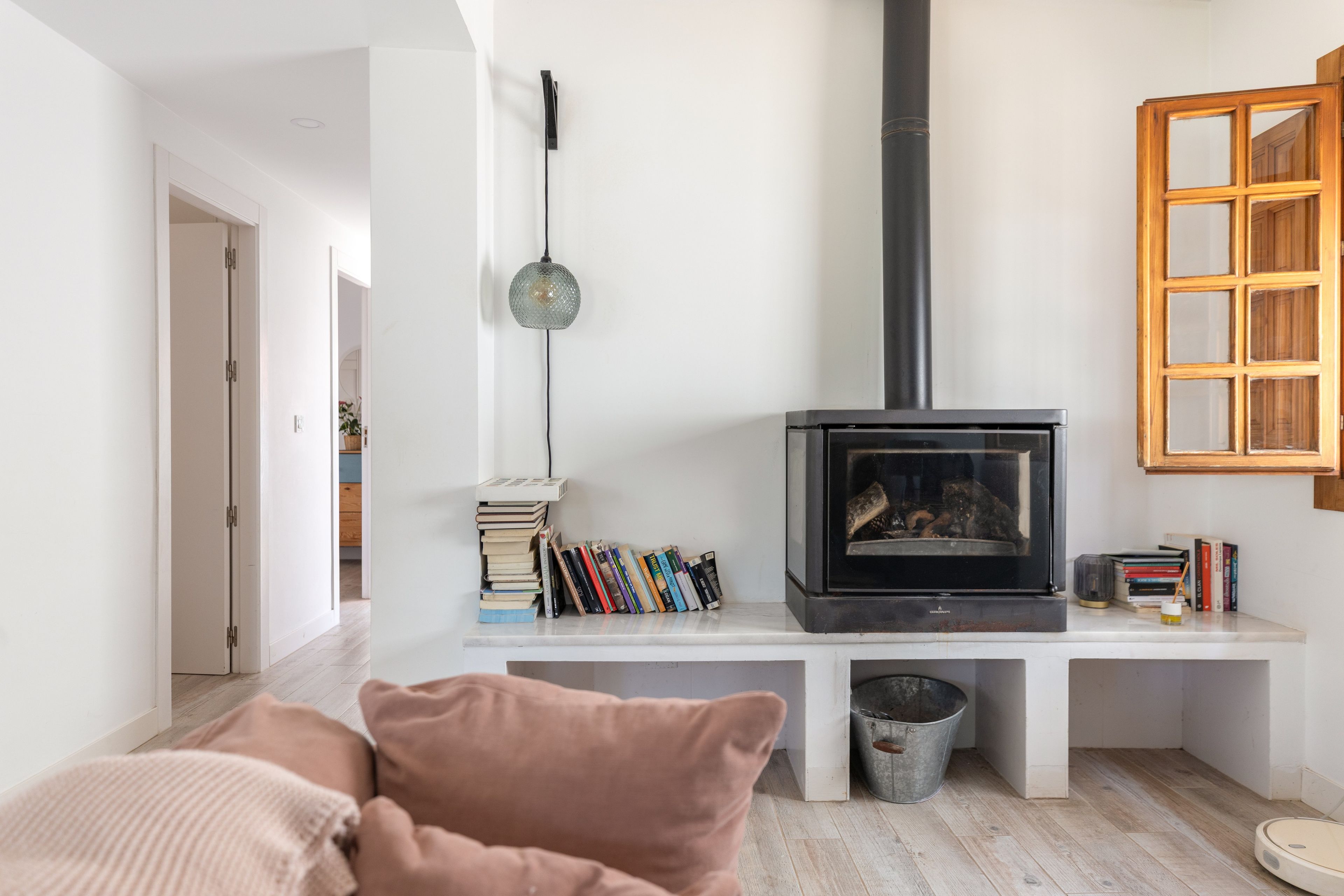 A living room with a wood-burning stove, bookshelves, a sofa, and a window with a wooden frame.