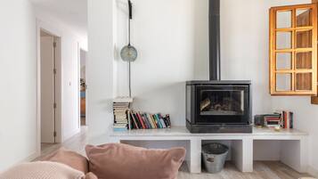 A living room with a wood-burning stove, bookshelves, a sofa, and a window with a wooden frame.