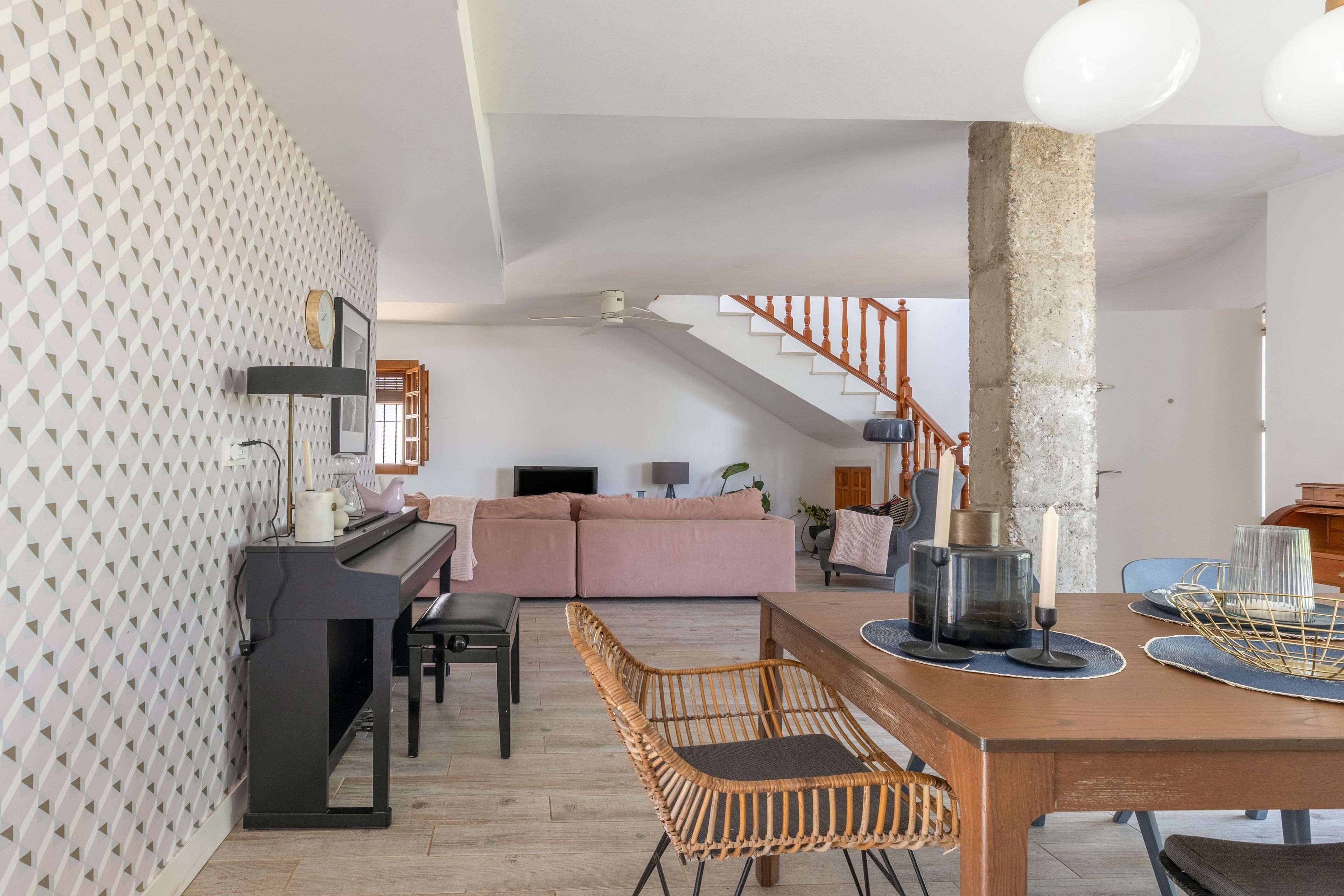Una sala de estar moderna con un piano, una mesa de comedor con sillas, una escalera y un pilar grande.