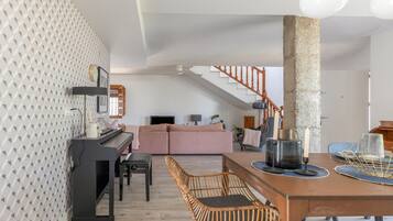 Una sala de estar moderna con un piano, una mesa de comedor con sillas, una escalera y un pilar grande.