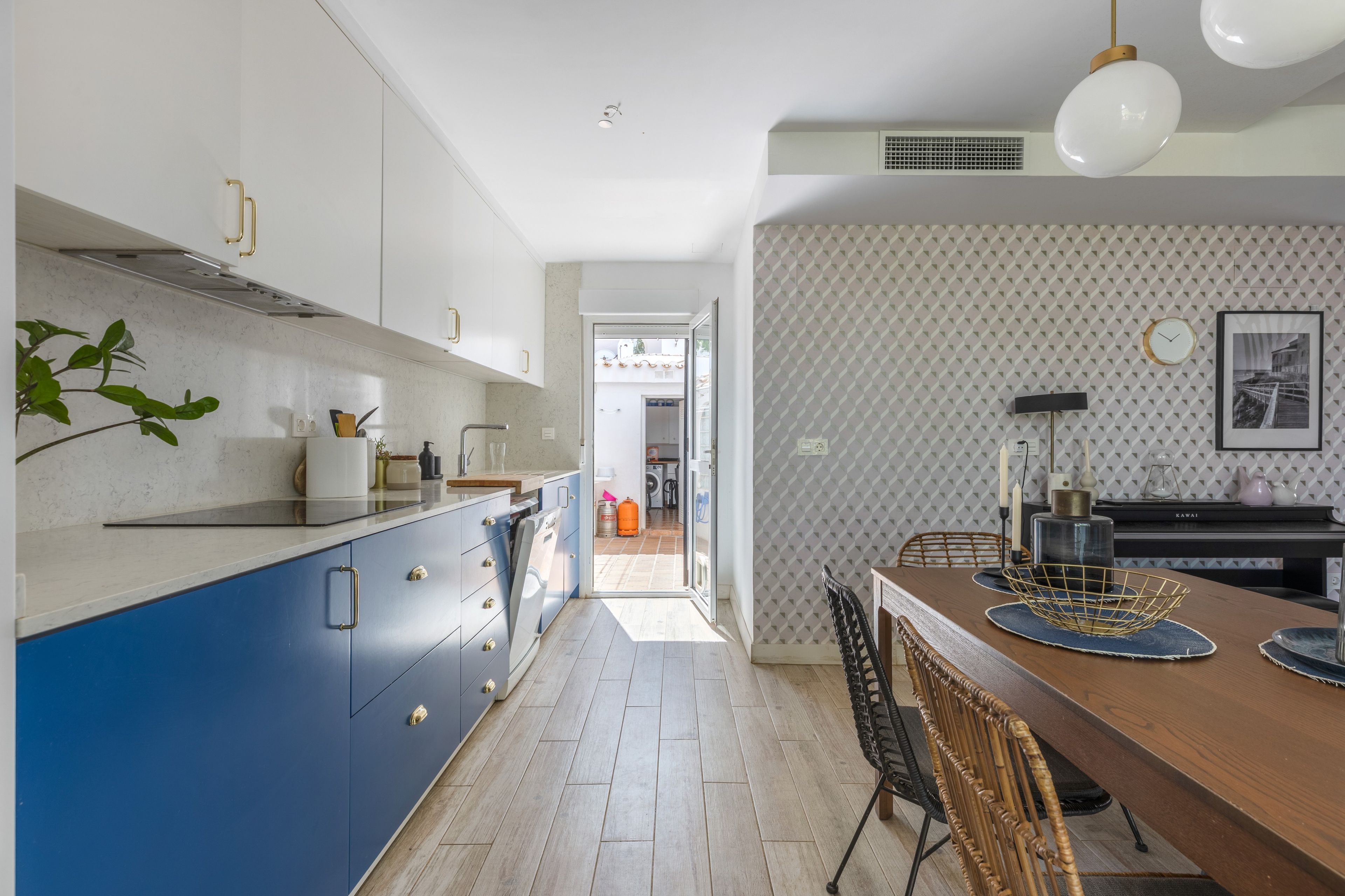 Une cuisine moderne avec des meubles de rangement bleus, une table à manger en bois et un mur orné d’un motif.